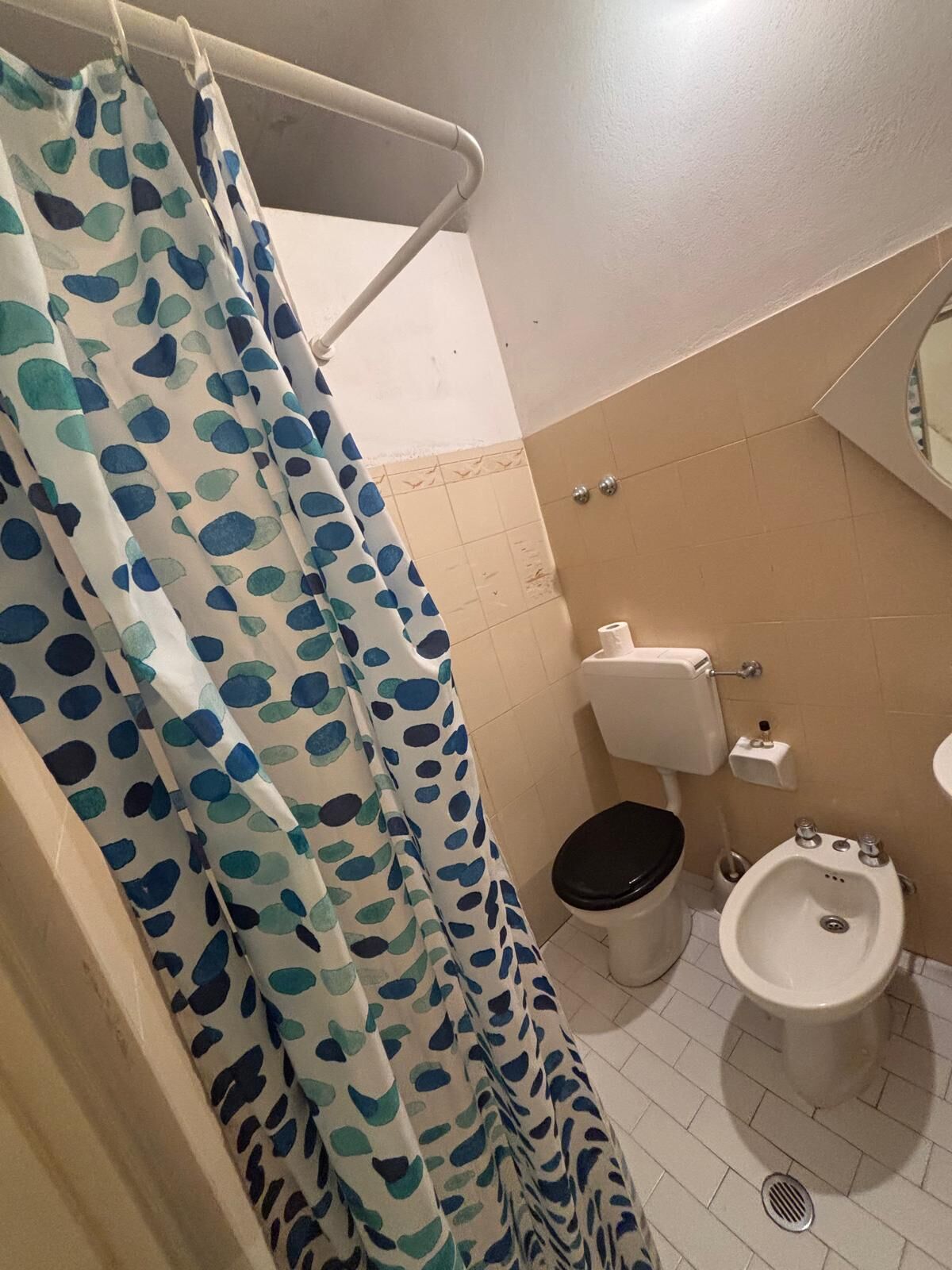 Ein Badezimmer mit Toilette, Bidet und einer Duschvorhang mit Blättermuster.