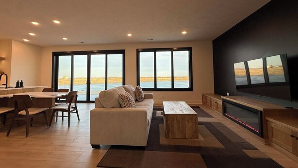 A modern living room with a large sofa, a dining area, and a TV mounted on the wall. - Private Waterfront Lake House Near Omaha (Valley)