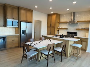 A modern kitchen with wooden cabinets, stainless steel appliances, a marble island, and bar stools.