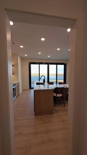 A modern kitchen with a large island, a dining area with a view, and a spacious room with wooden flooring.