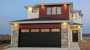 A two-story house with a black garage door, stone pillars, and a red and white exterior. - Private Waterfront Lake House Near Omaha (Valley)