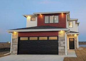 A two-story house with a black garage door, stone pillars, and a red and white exterior.
