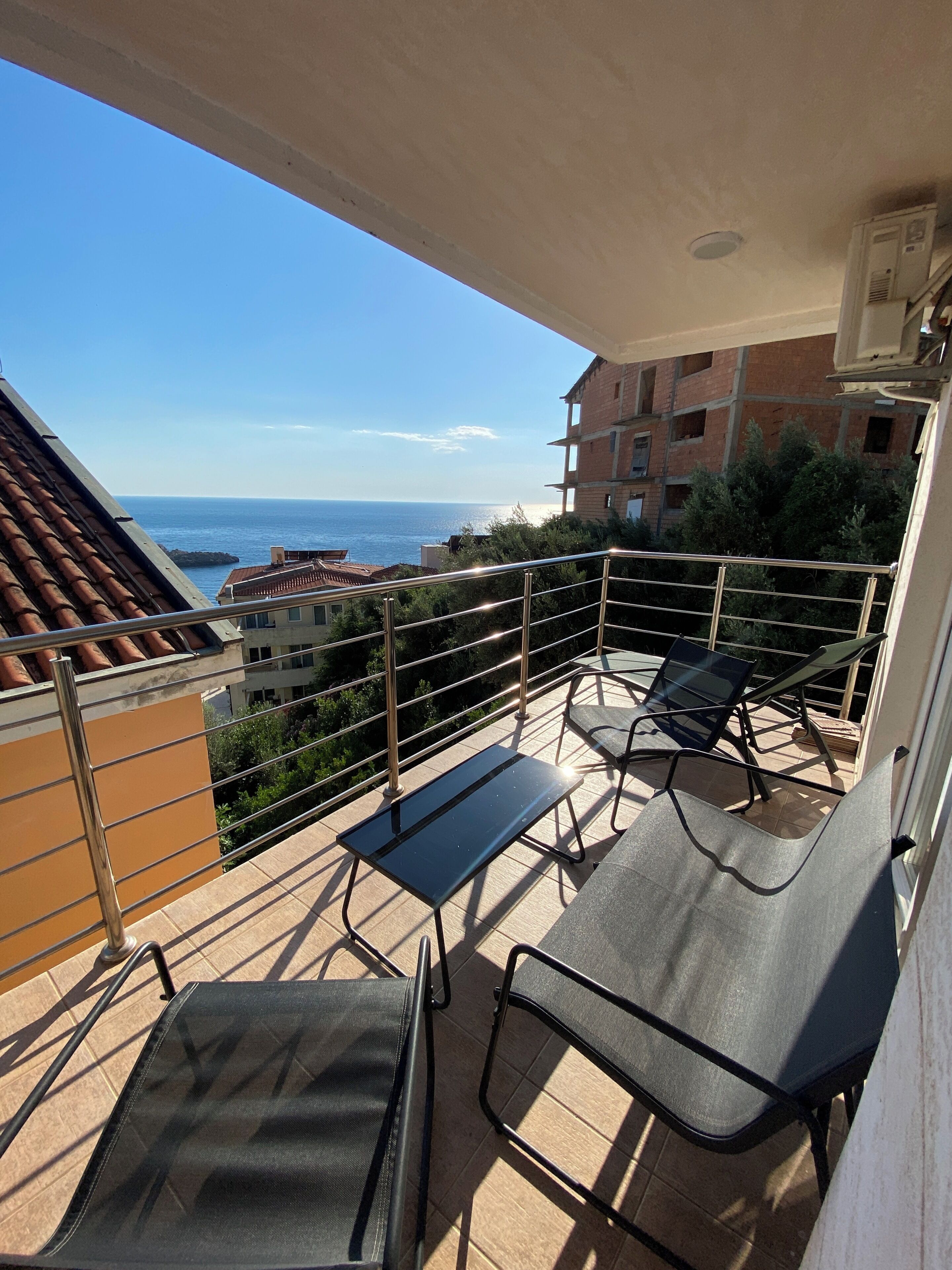 Un balcon avec deux chaises et une table, offrant une vue sur la côte et sur des bâtiments en arrière-plan.