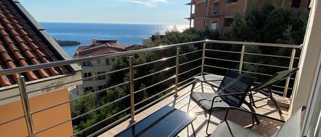 Un balcon avec deux chaises et une table, offrant une vue sur la côte et sur des bâtiments en arrière-plan.
