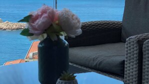 Una mesa de vidrio con un florero y una planta pequeña, un sofá gris y vistas al mar.