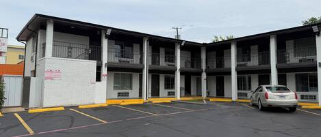 A multi-story parking garage with a white building facade, multiple parking spaces, and a silver car parked in one of the spaces.