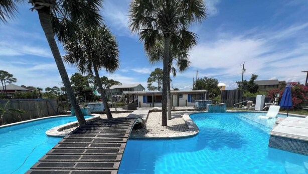 Piscina com deck de madeira, palmeiras e céu azul límpido.