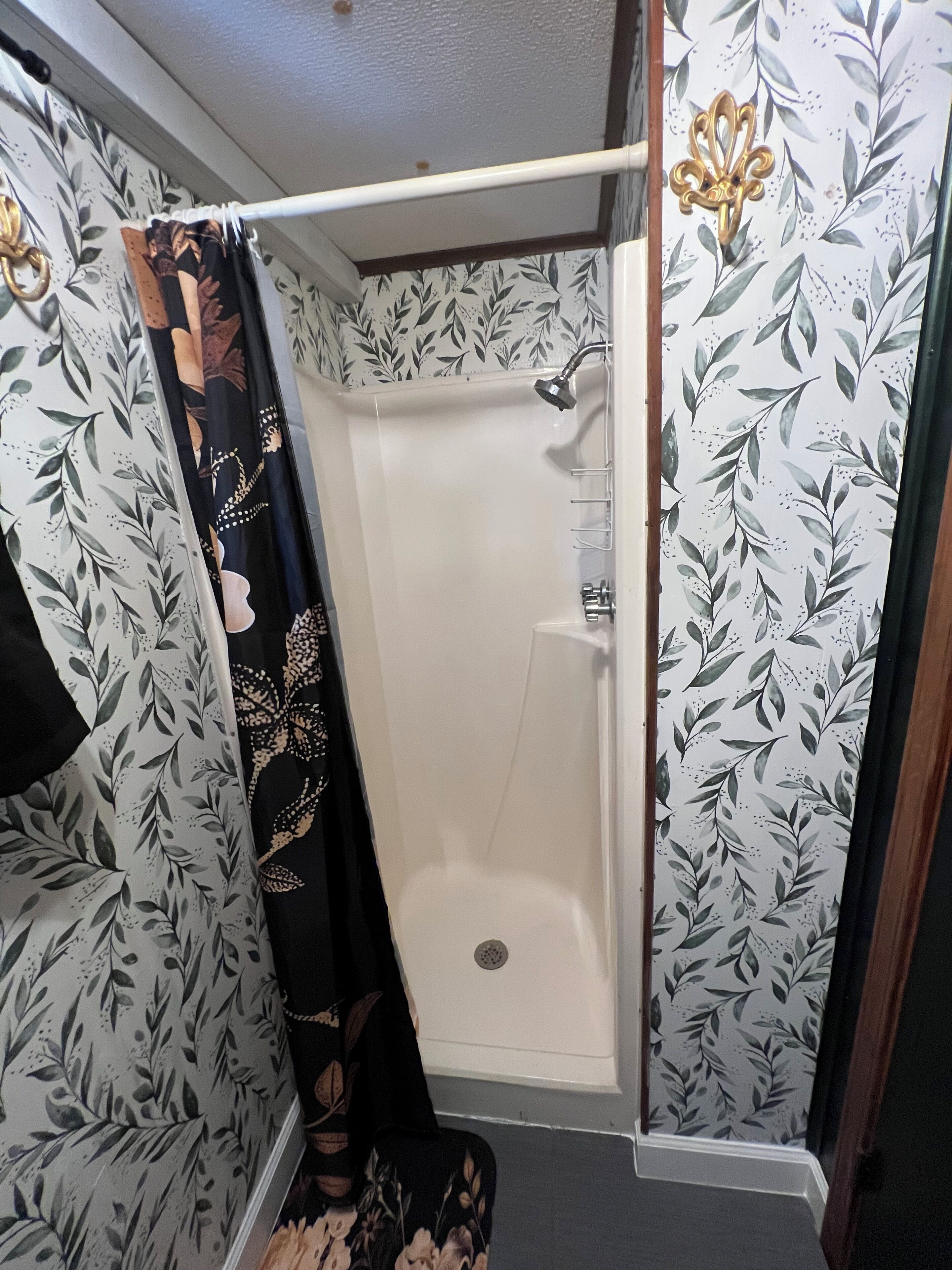 A shower area with a white showerhead, a glass door, and a shower curtain with a floral pattern.