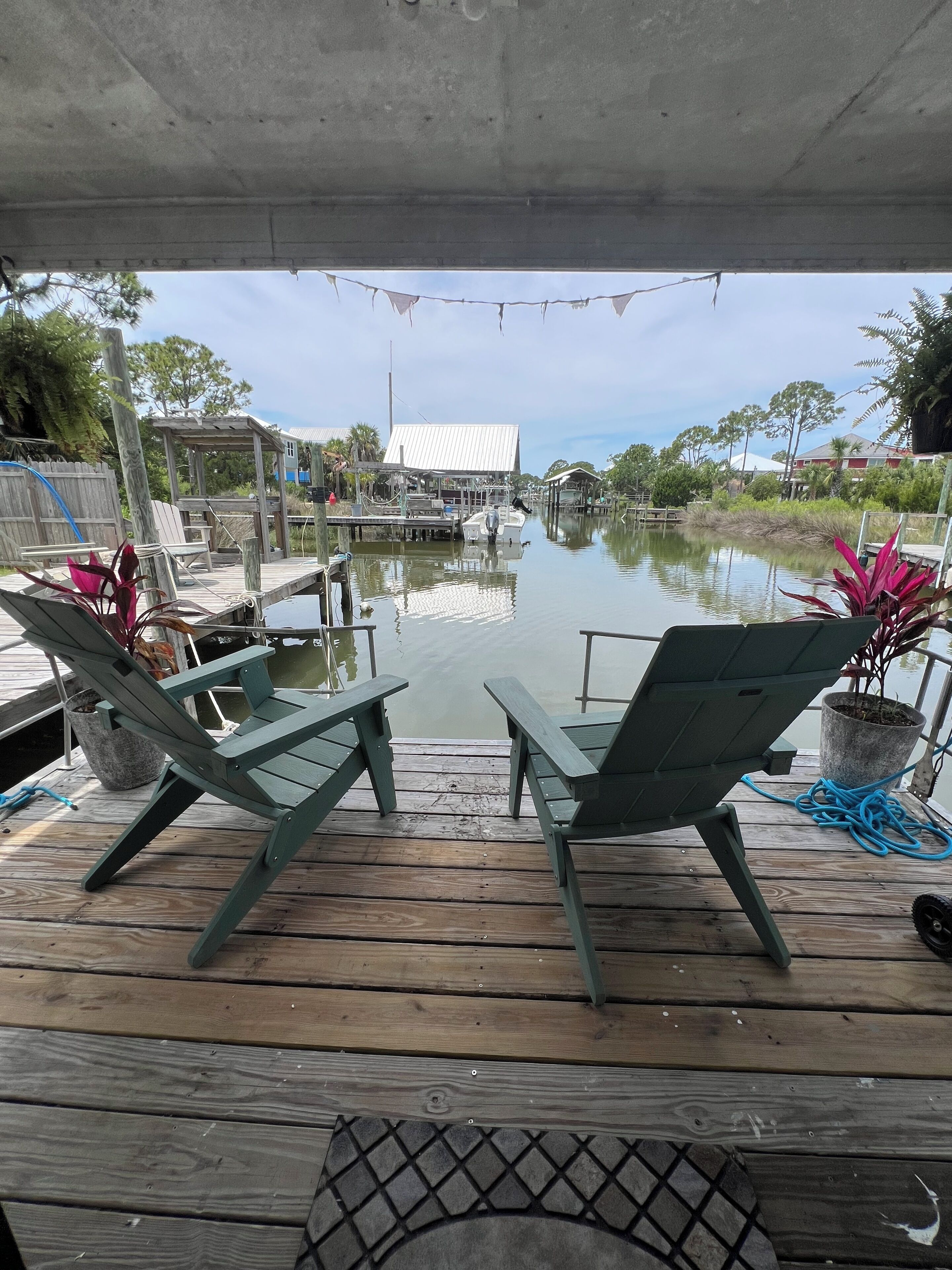 A wooden deck with two green chairs, a small table, and a potted plant.