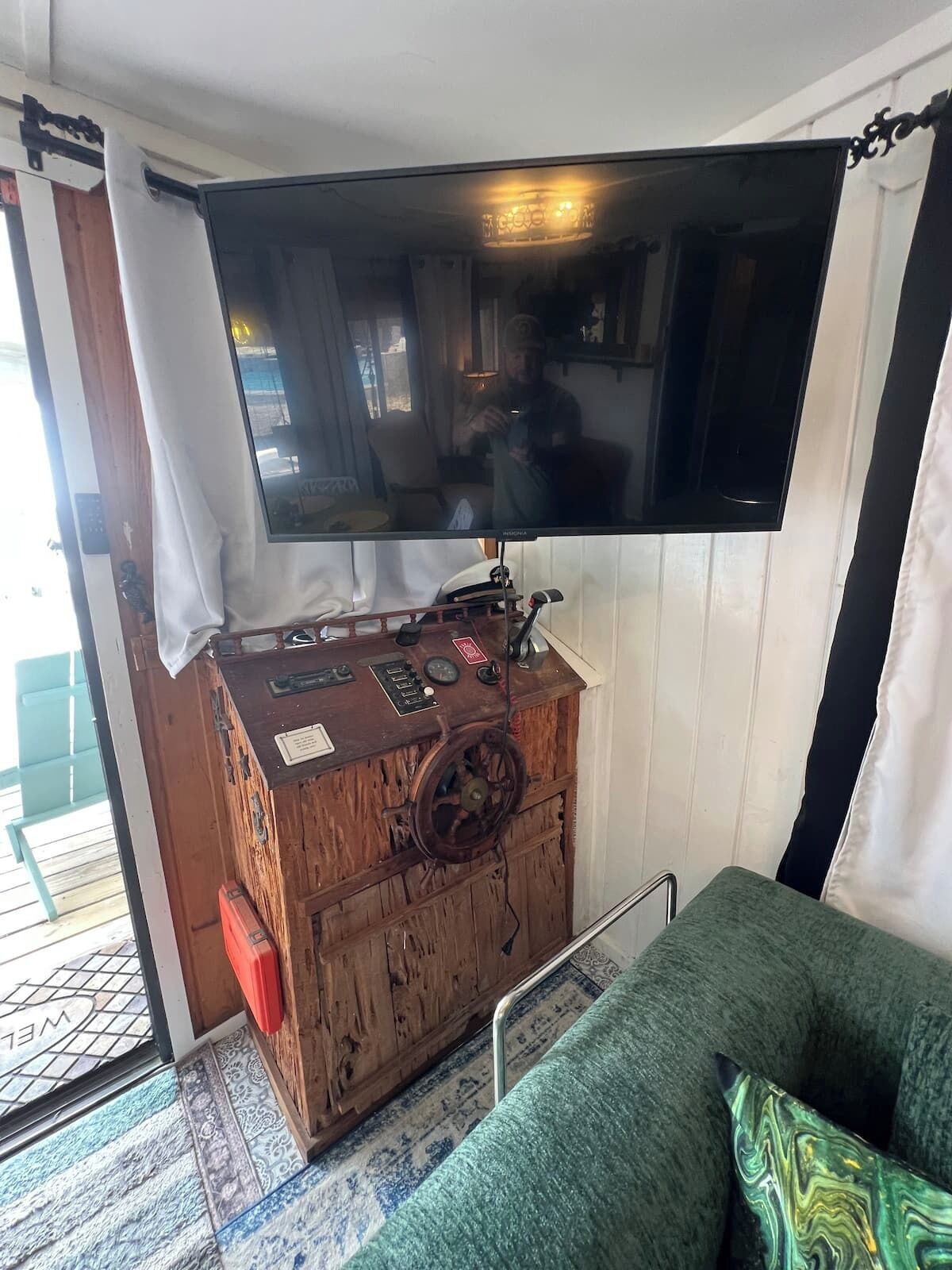 Une pièce avec un téléviseur fixé sur un meuble en bois, un canapé vert et un tapis à motifs.