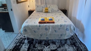 Quarto de hotel com cama, mesa de cabeceira, luminária, espelho e luminária no teto.