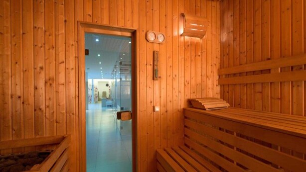 A wooden sauna room with benches, a glass door leading to a hallway, and a wall-mounted thermometer. - 2 Person Holiday Park Home in Brauschweig (Braunschweig)