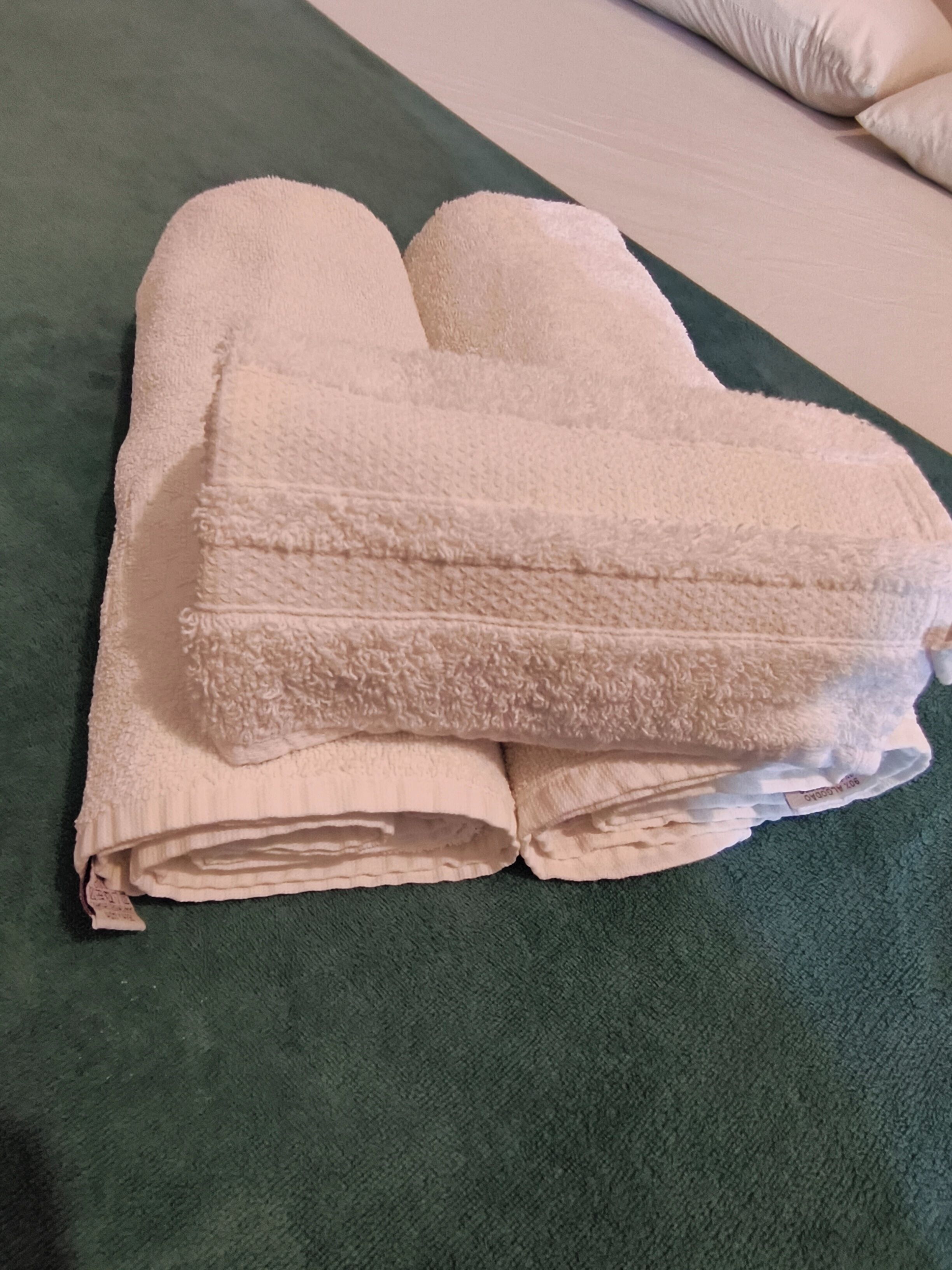 A stack of folded towels on a green bedspread.