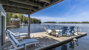 A wooden dock with lounge chairs and a table, overlooking a calm lake with a forested shoreline. - 6 bed 5 bath cottage on Lake Rosseau (Nipissing South (Utterson))