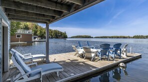 Un muelle de madera con sillones de descanso y una mesa, con vista a un lago tranquilo bordeado por un bosque.