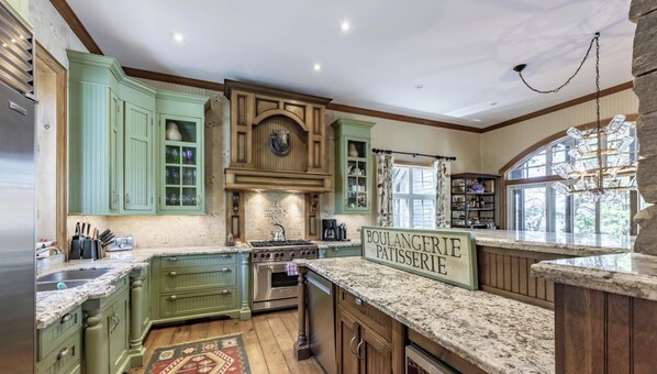 A kitchen with green cabinets, a stone countertop, a stove, and a sign that reads 'BOULANGERIE PATSERIE.' - 6 bed 5 bath cottage on Lake Rosseau (Nipissing South (Utterson))