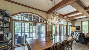 A spacious dining area with a wooden table and chairs, large arched windows, and a chandelier. - 6 bed 5 bath cottage on Lake Rosseau (Nipissing South (Utterson))