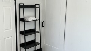 A room with a black metal shelf unit against a white door, a wooden floor, and a white wardrobe.