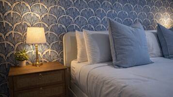 A bedroom with a patterned wallpaper, a bedside table with a lamp, and a bed with pillows.
