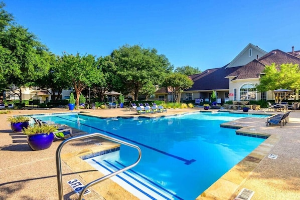 A swimming pool with lounge chairs, potted plants, and a building with a tiled roof in the background.
