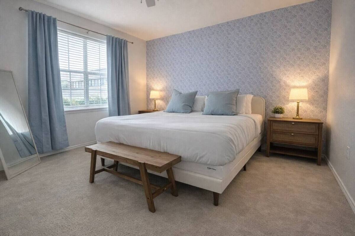 A bedroom with a bed, bedside tables, a bench, and a window with curtains.