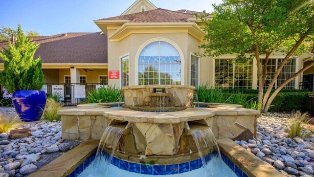 A swimming pool with a waterfall feature, surrounded by a stone deck and a large blue planter.