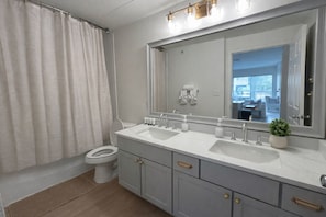 A bathroom with a toilet, two sinks, a large mirror, and a potted plant.