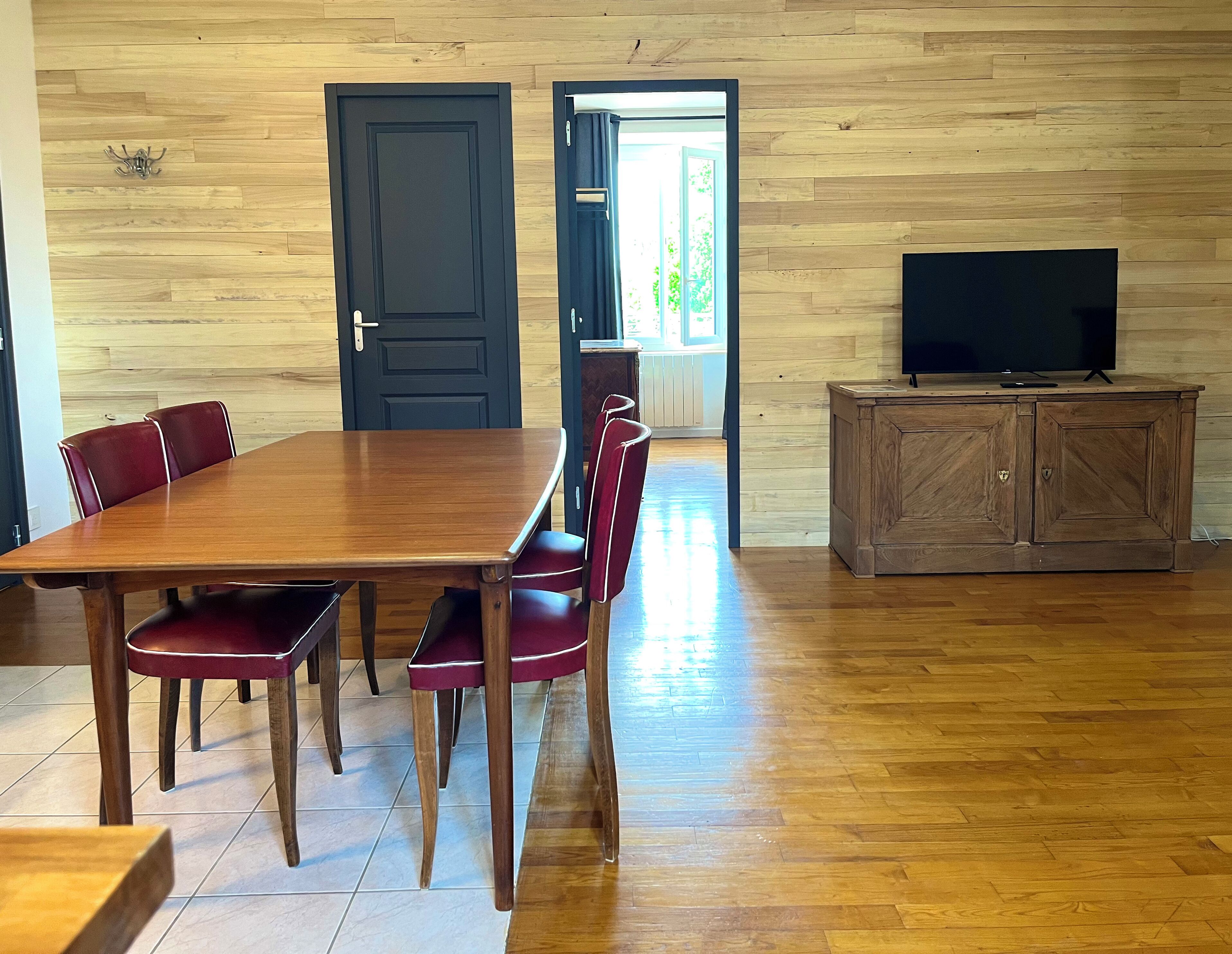 A dining area with a wooden table and chairs, a television on a cabinet, and a door leading to another room.