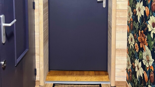 A dark blue door with a silver handle, a wooden door frame, and a welcome mat at the entrance.