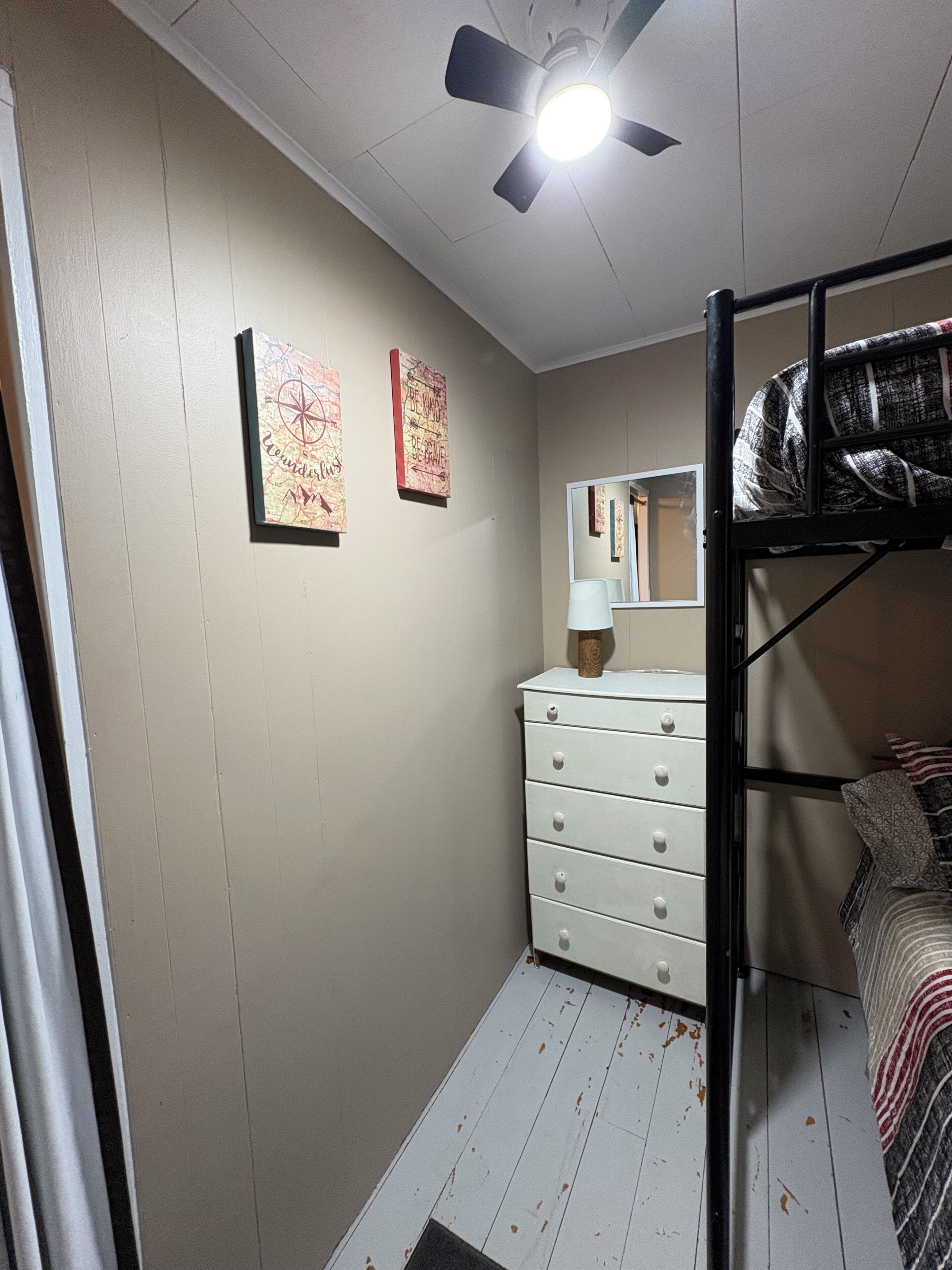 A bedroom with a bunk bed, a dresser, a ceiling fan, and two wall-mounted artworks.