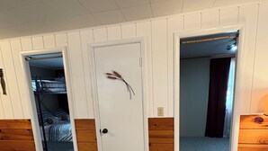 A room with a bunk bed, a desk, a chair, and a door with a decorative item.
