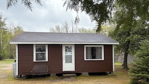 A small, single-story house with a brown exterior and white trim, a front door, and two windows.