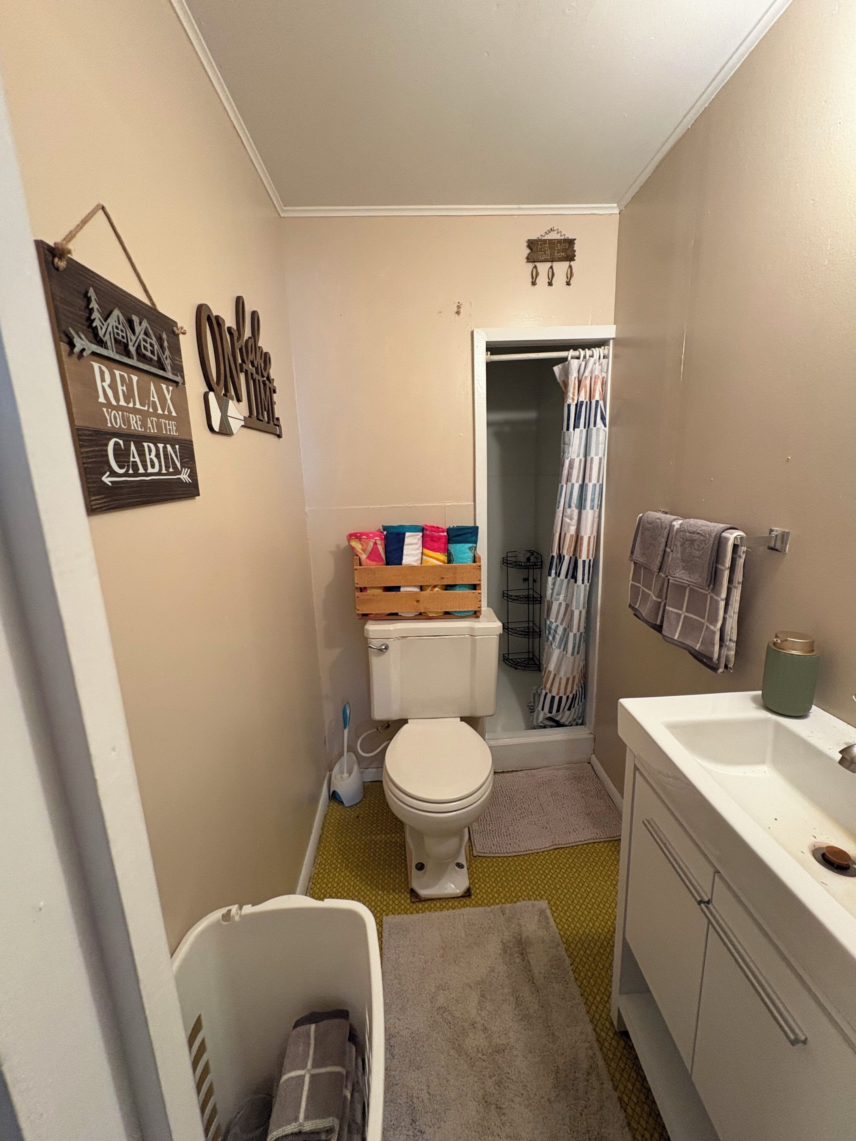 A compact bathroom with a toilet, a sink, a shower curtain, and a small storage area with folded towels.