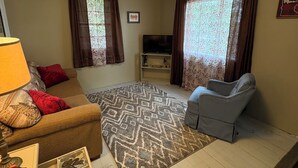 A living room with a sofa, a chair, a TV, a lamp, and a patterned rug.
