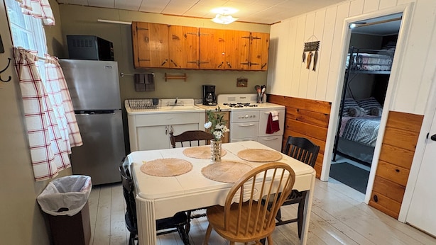 A compact kitchen with wooden cabinets, a refrigerator, a coffee maker, and a dining table with placemats.