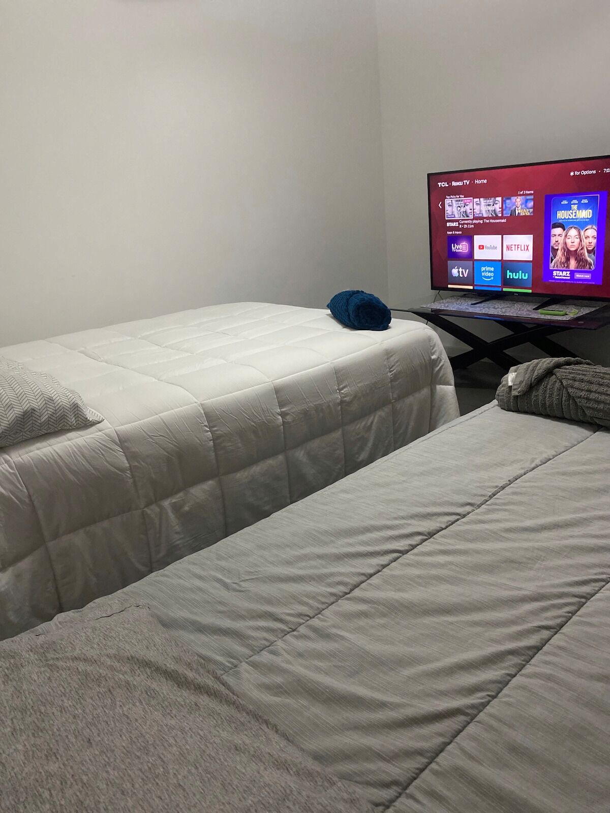 Habitación de hotel con dos camas, un televisor mostrando la interfaz de una plataforma de streaming y una mesita con un control remoto.