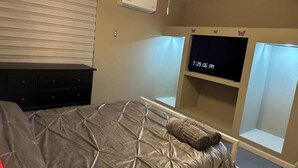 A bedroom with a bed, a TV, a dresser, and an air conditioning unit.