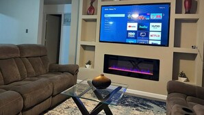 A living room with a flat-screen TV mounted on the wall, a fireplace below it, and two brown sofas.