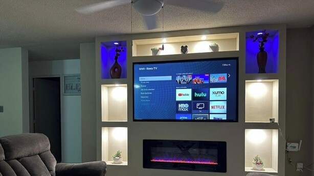 A living room with a flat-screen TV mounted on the wall, a fireplace below, and two sofas.