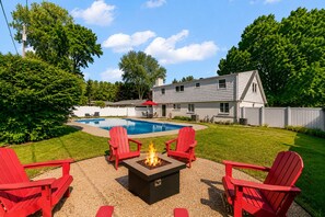 A backyard with a swimming pool, red Adirondack chairs, and a fire pit. - Timber & Tides : St Joseph : Beautiful Home : Pool & Game Room : Family Friendly (St. Joseph)