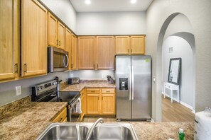 Eine Küche mit Holzschränken, Edelstahlgeräten, Granit Arbeitsplatten und einer weißen Wand mit rundbogenförmigem Durchgang.
