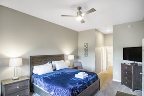 Ein Schlafzimmer mit Bett, Nachttischen, Schreibtisch, Fernseher und Deckenventilator.