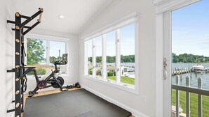 Una palestra con attrezzature per esercizi, un tappetino da yoga e vista su un lago attraverso ampie finestre.