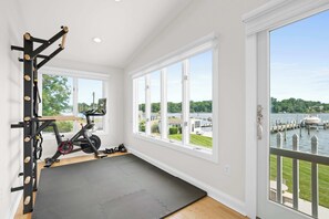 Ein Fitnessraum mit Trainingsgeräten, einer Yogamatte und Blick auf einen See durch große Fenster.
