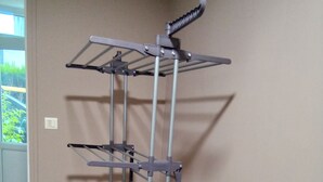 A metal drying rack with multiple shelves against a wall, a tiled floor, and a door leading outside. - Champagne character apartment (Essoyes)