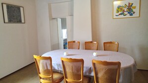 A dining room with a round table, six wicker chairs, a white tablecloth, two white candles, and a colorful abstract painting on the wall. - Champagne character apartment (Essoyes)
