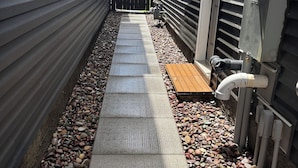 A narrow pathway with a textured surface, flanked by metal siding walls and a wooden deck. - 10 minutes from the YYC airport! Modern basement suite with all facilities (Calgary)