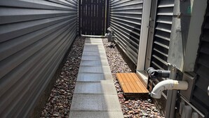 A narrow pathway with a textured walkway, surrounded by metal siding walls and a wooden fence. - 10 minutes from the YYC airport! Modern basement suite with all facilities (Calgary)