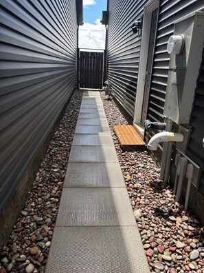 Ein schmaler Weg mit strukturierter Laufbahn, umgeben von Wänden aus Metallverkleidung und einem Holzzaun.