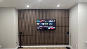 A modern living room with a flat-screen TV mounted on a wooden panel wall, a glass coffee table, and a patterned rug. - 10 minutes from the YYC airport! Modern basement suite with all facilities (Calgary)